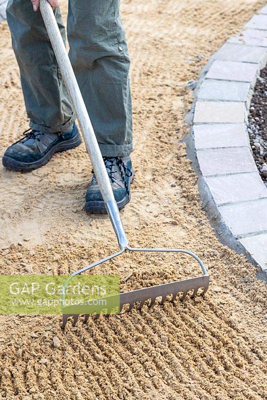 Man raking out course sand base for gravel path