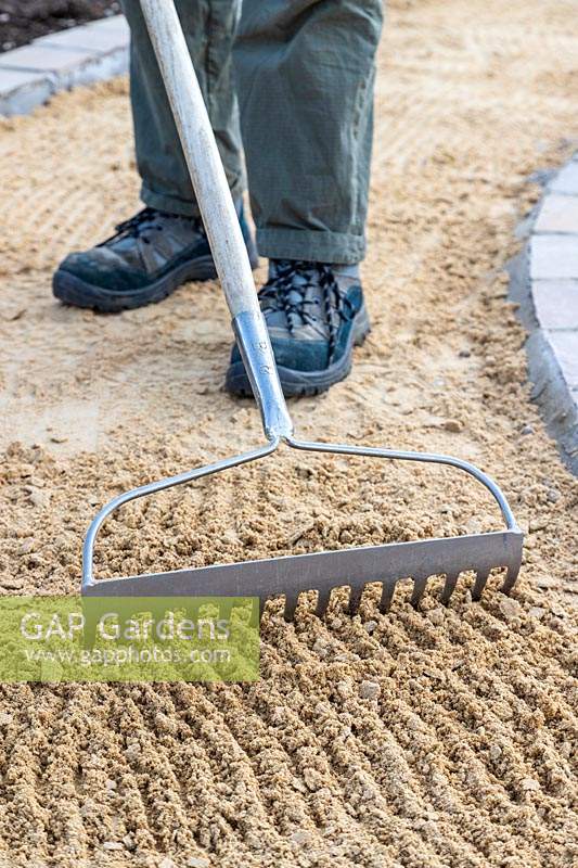 Man raking out course sand base for gravel path
