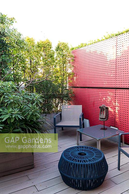 A red partition with seating in front, decked surface with plant screens in troughs 