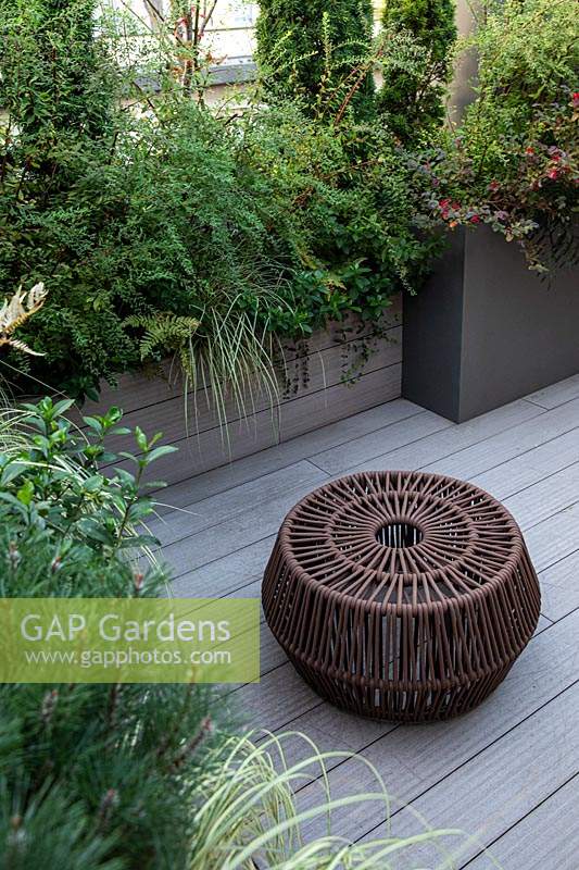 Decked roof garden with fireplace transformed into a sculpture, mixed planting in troughs provides a screen 