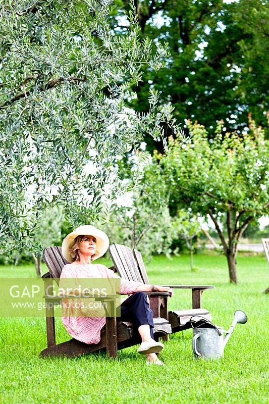 Woman sitting on Adirondack chair on a lawn, trees nearby