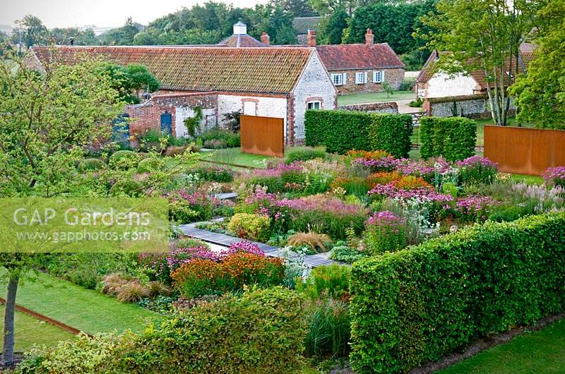 Overview of modern formal country garden, flower beds in blocks surrounded by hedges with view of buildings beyond