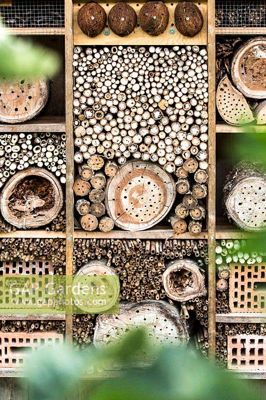 Insect house made by filling a grid of wood with sticks, logs with holes and bricks