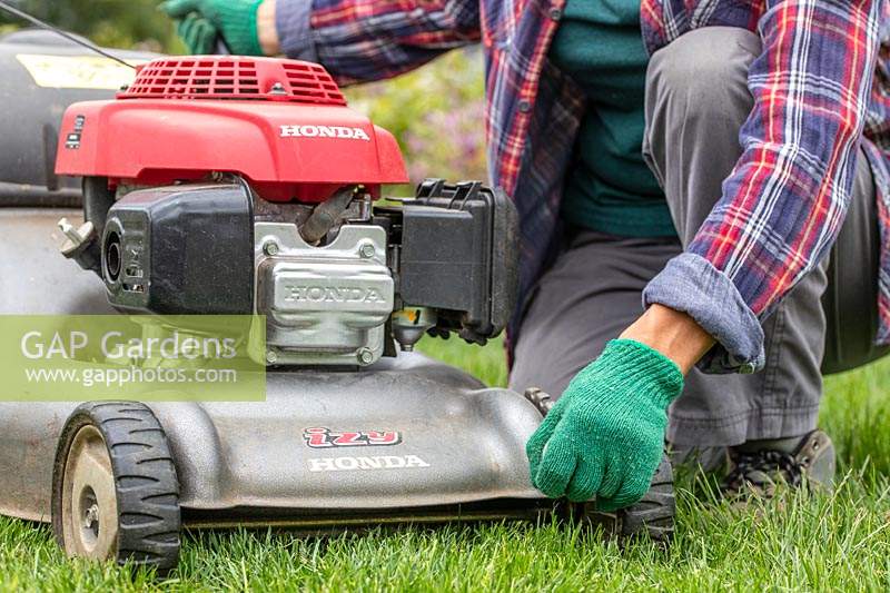 Woman adjusting the cutting height of a rotary lawnmower