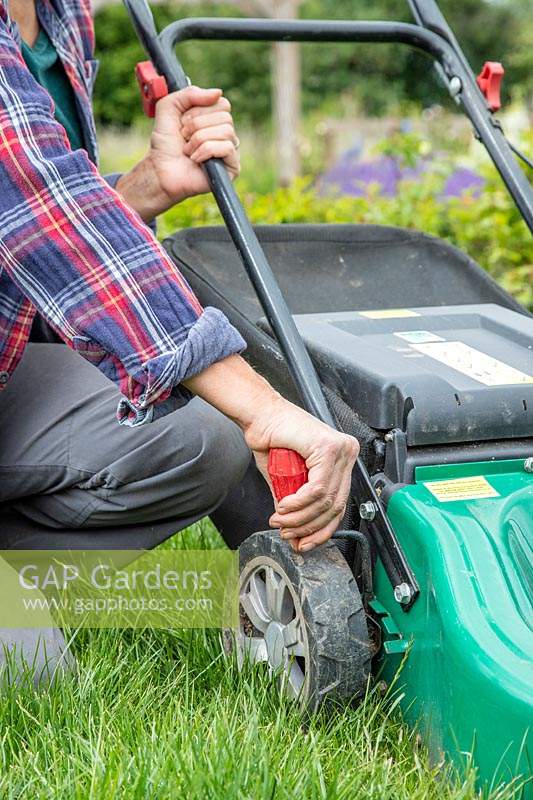 Woman adjusting the cutting height of a rotary lawn mower in long grass