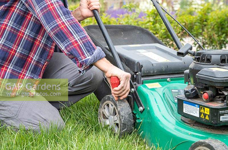 Woman adjusting the cutting height of a rotary lawn mower in long grass