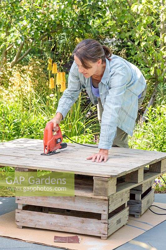 Woman using electric jigsaw to cut up a wooden pallet