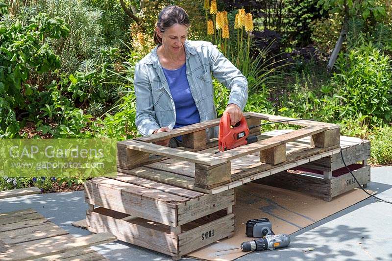 Woman using an electric jigsaw to cut a whole in the middle of a pallet
