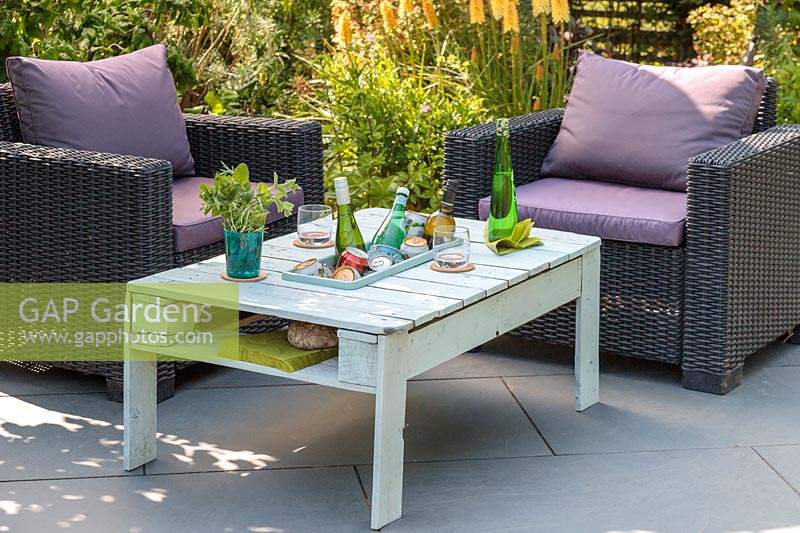 Outdoor chairs by wooden pallet table, with integral drinks cooler on slate patio in summer set up for a party. 