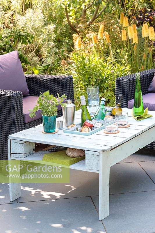 Outdoor chairs by wooden pallet table , with integral drinks cooler on slate patio in summer set up for a party.
