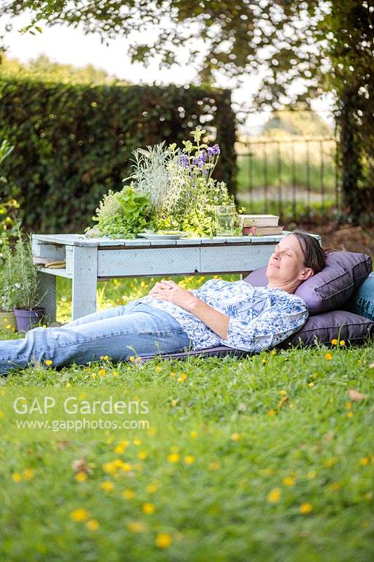 Woman relaxing on purple cushions, next to a wooden table with integral herb planter. 