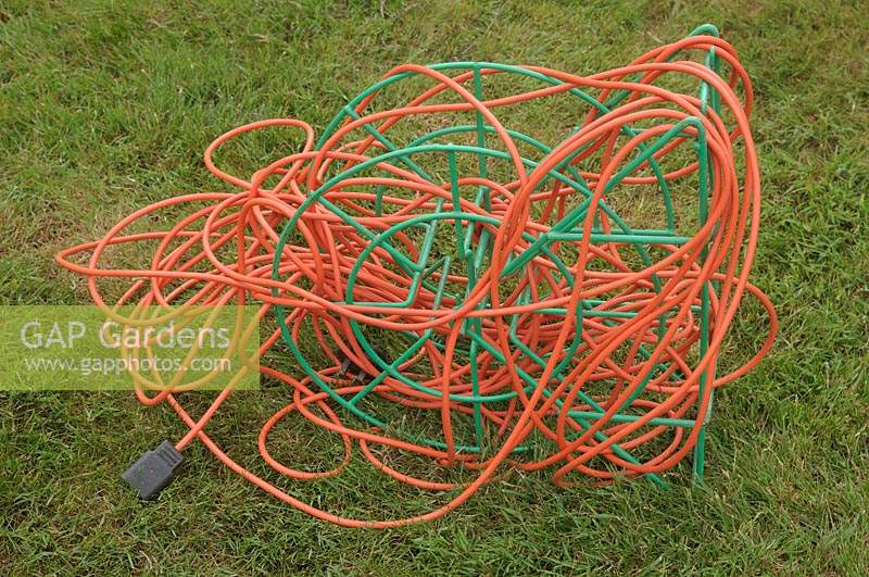 Heavily tangled orange power cord extension lead wrapped around a metal frame