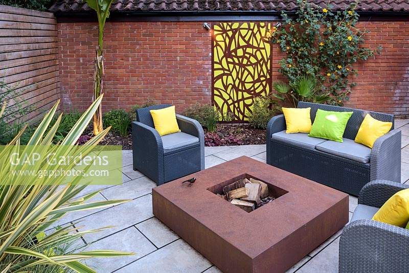 Sofa and armchairs around fire pit in small modern garden