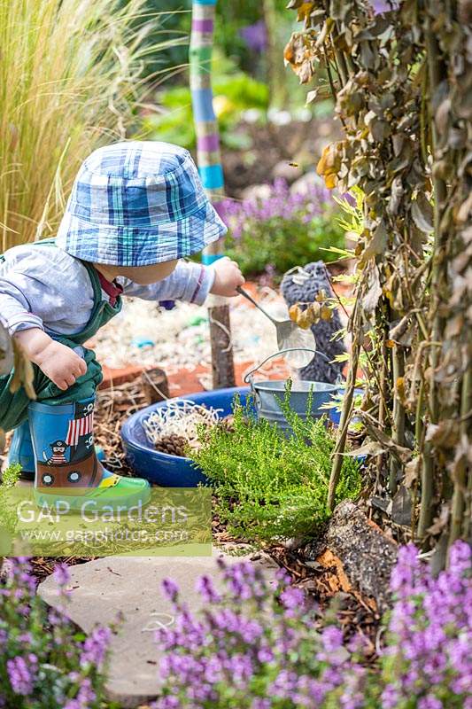 Young toddler playing with spoon and bucket in sensory garden