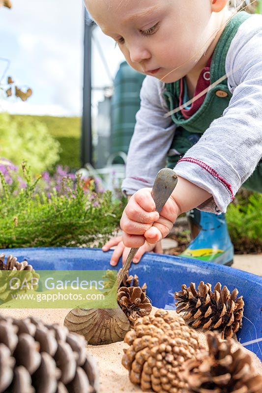 Young toddler playing with spoon, sand and pine cones in sensory garden