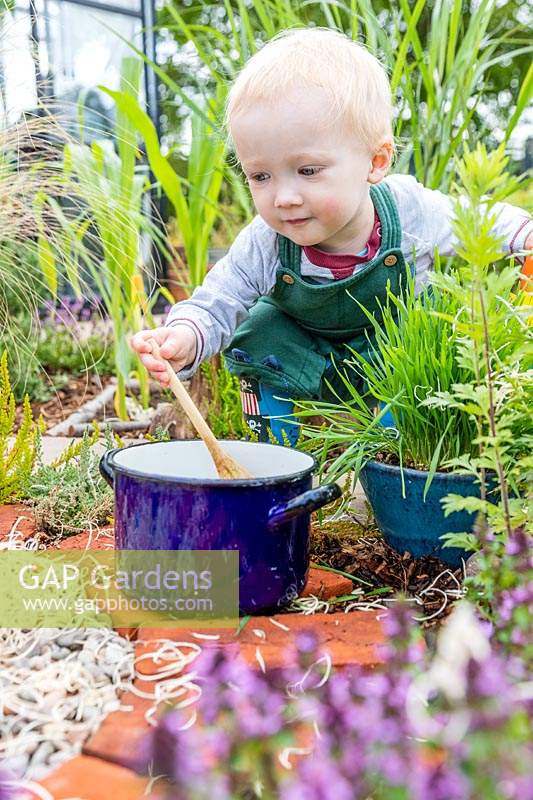 Young toddler playing with saucepan and wooden spoon in sensory garden