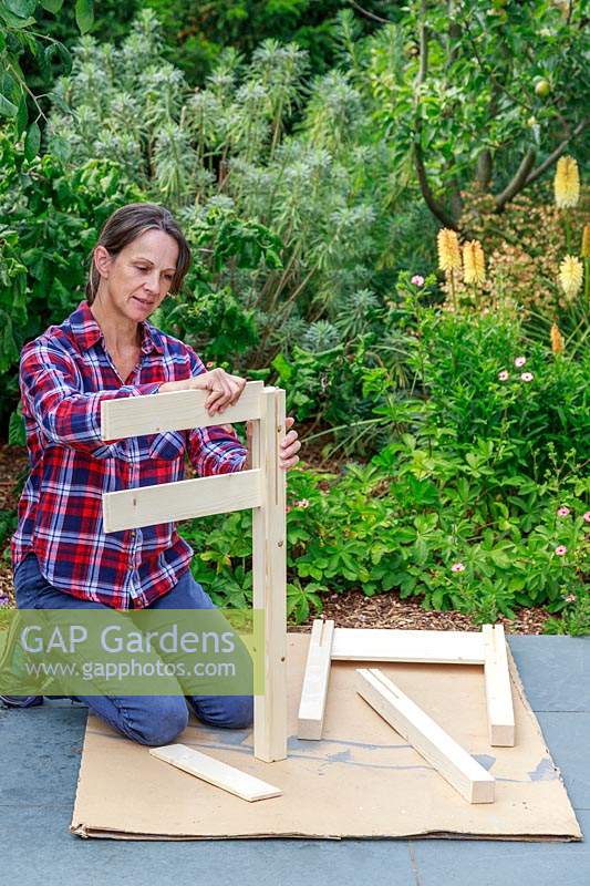 Woman inserting side panels for a raised planter being built from a kit