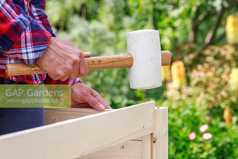 Close up detail of using a soft rubber mallet to insert wooden side panels into a pre-cut grove