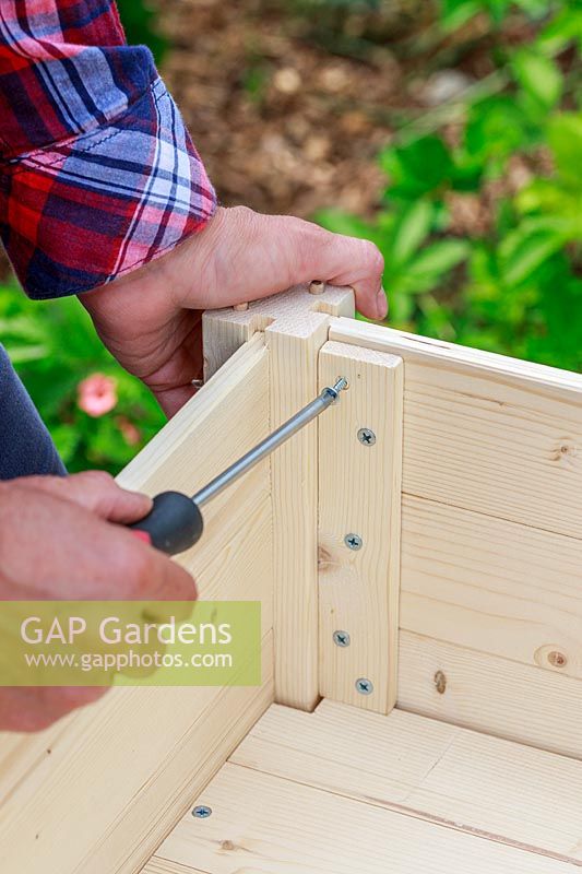 Using a screw driver to screw together wooden panels of a raised planter built from a kit