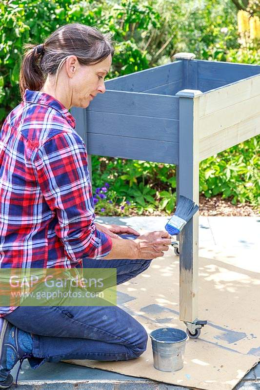 Woman painting a wooden raised planter with grey paint