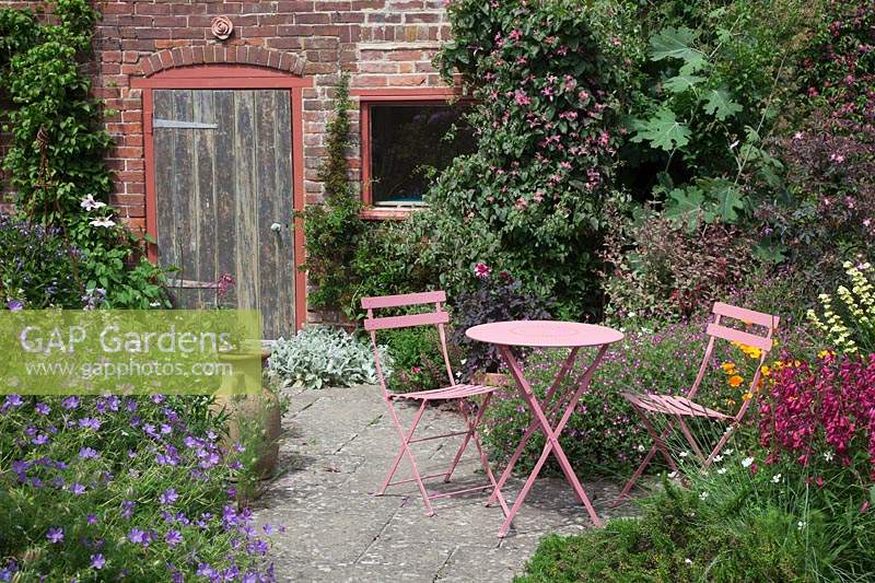 Pink metal table and chairs by brick potting shed in small paved courtyard.