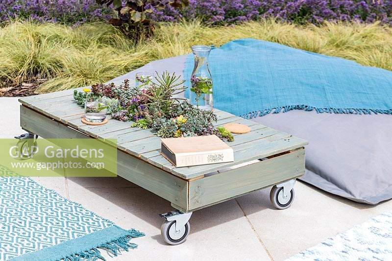 Finished pallet table with succulents on patio with rugs and beanbag seating. 