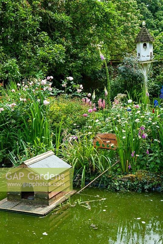 Duck house on pond with marginal plants and perennial border with dovecote beyond - Open Gardens Day, Great Finborough, Suffolk