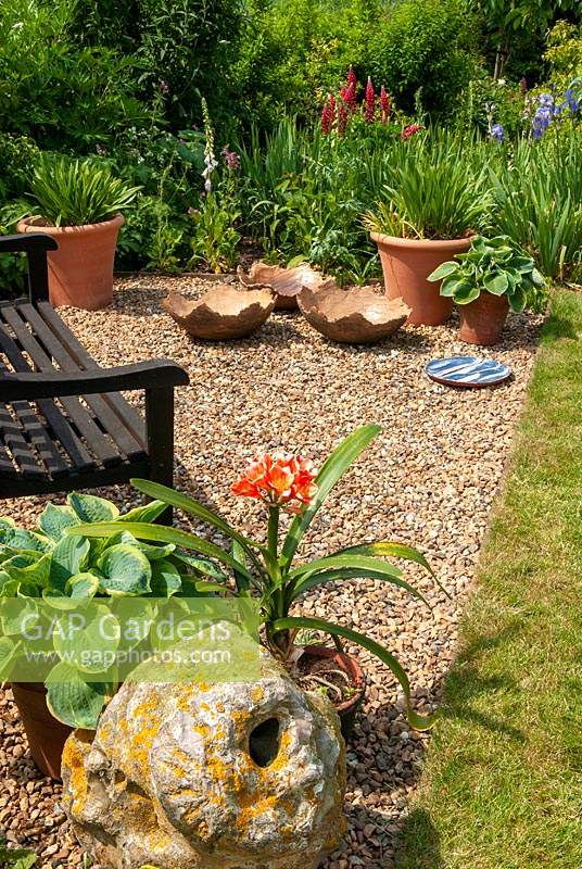 Garden seat on gravel with container grown Hostas and Amaryllis belladonna - Easter Lilly - and ornamental bowls - Open Gardens Day, Palgrave, Suffolk