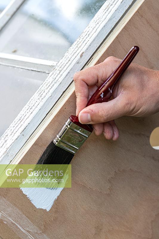 Man painting coldframe using a paint brush