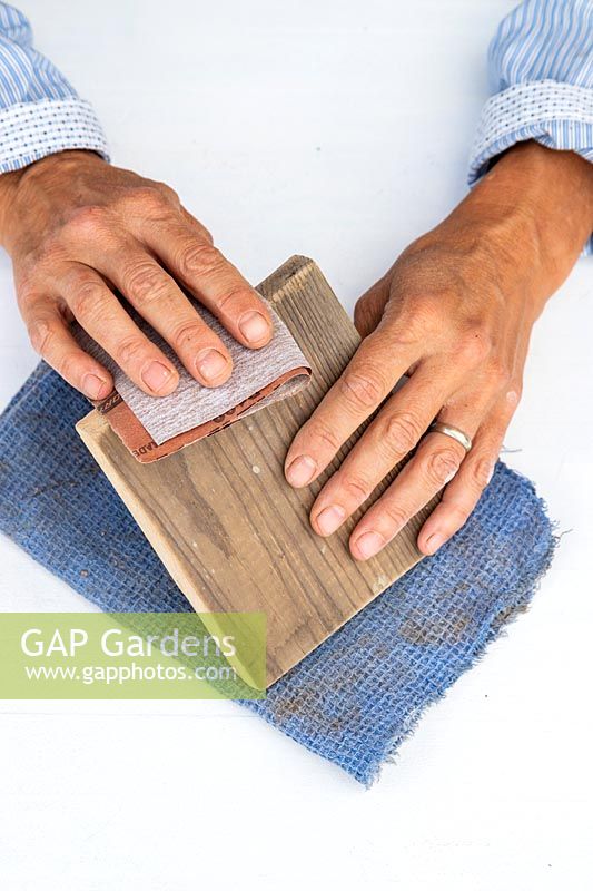 Woman using sandpaper to smooth the edges of the piece of timber which will be used as a shelf