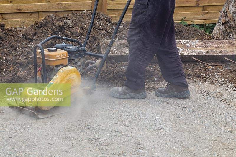 Man compressing foundation of crushed concrete for patio with compaction plate. 