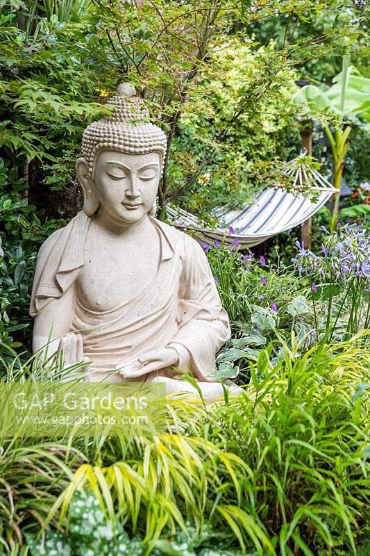 Buddha sculpture in small garden with exotic planting