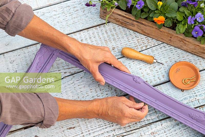 Woman fixing an eyelet to the side of painted purple picture frame
