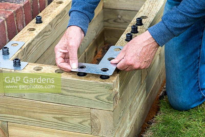 Person building raised bed: fixing an angle plate to each corner for additional stability.