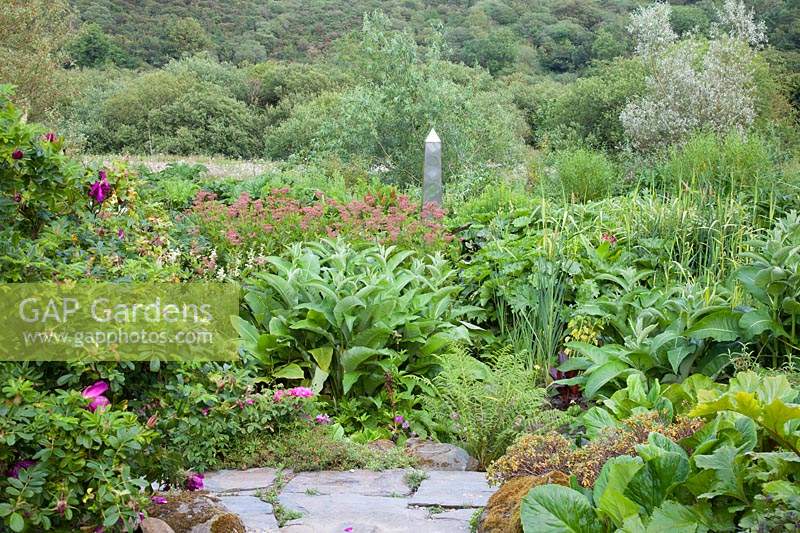 Decorative metal obelisk feature amongst dramatic summer planting with Welsh countryside beyond