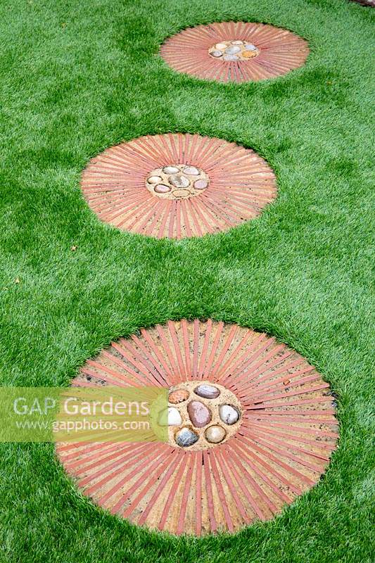 Circular terracotta path steps with pebbles at centre set in artificial lawn