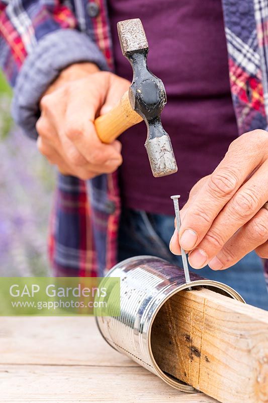 Woman using a hammer, nail and a piece of timber to create a hole in the side for hanging up the tin can