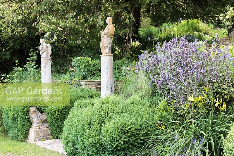 A marble lion below columns topped by Sienese saints from the 15th century, arising from mature shrubby Salvia rosmarinus - Rosemary - with Salvia - Sage nearby 