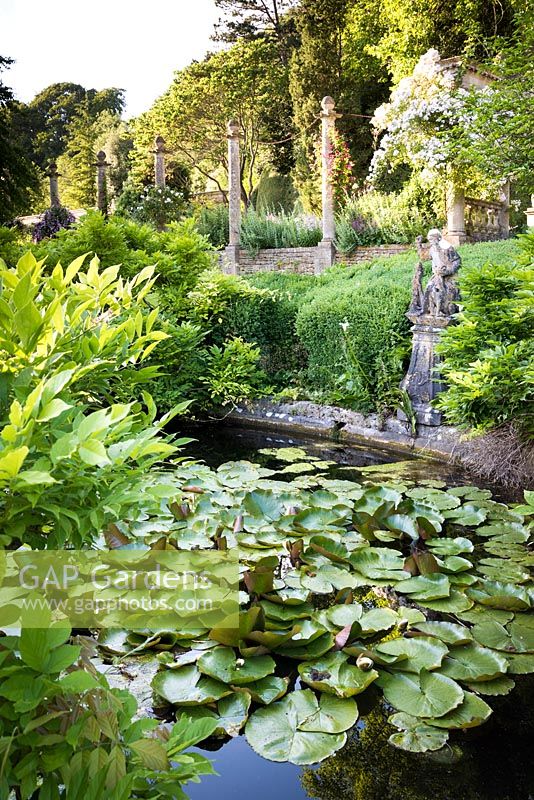 Waterlily pond with 16th century figure of a huntsman at edge, view of trees and architecture beyond