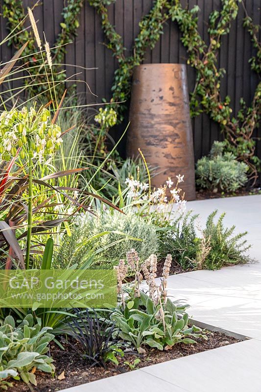 White zig zag paving with mixed planting and view to large pot in background. 