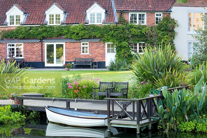The 'gin and tonic boat' is moored on the pontoon, behind the house with its wisteria-covered wall. Planting includes Phormium tenax and Thalia dealbata.