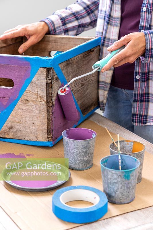 Woman using small roller to paint triangle sections on wooden box