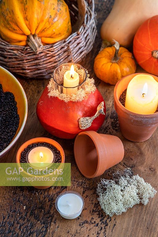 Table with various autumnal candle decorations, squashes, lichen, terracotta pots and black grit