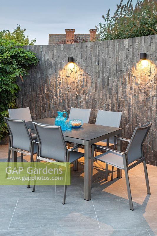 Modern dining furniture backed by slate covered wall and wall-mounted downlighters