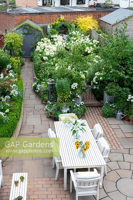 Bird's eye view of a small town garden, with dining and seating areas and white-themed borders.