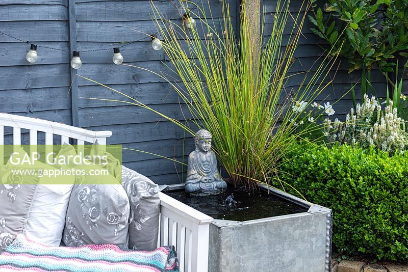 An old galvanised water tank  is converted into a bubbling water feature, planted with a clump of rushes.
