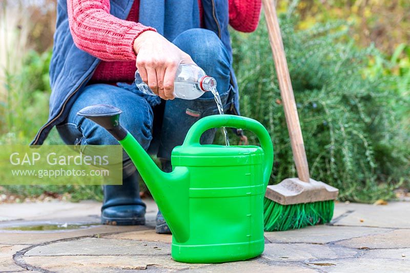 Woman adding white vingar to watering can so that the diluted mix can be used for cleaning paving