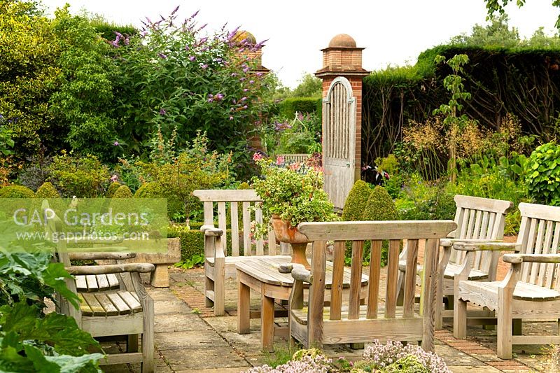 Teak furniture in a paved courtyard surrounded by a herbaceous borders at East Ruston Old Vicarage