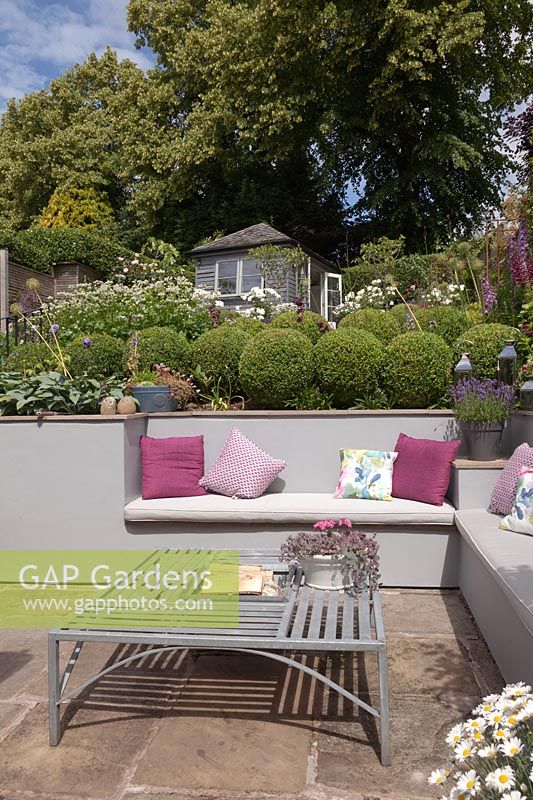 Sunken seating area in cottage garden with bench built in to retaining wall and fire-pit in metal table, Cheshire