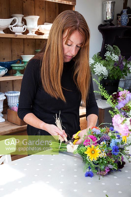Zelie in the flower studio making hand tied bunches of flowers and securing with raffia.